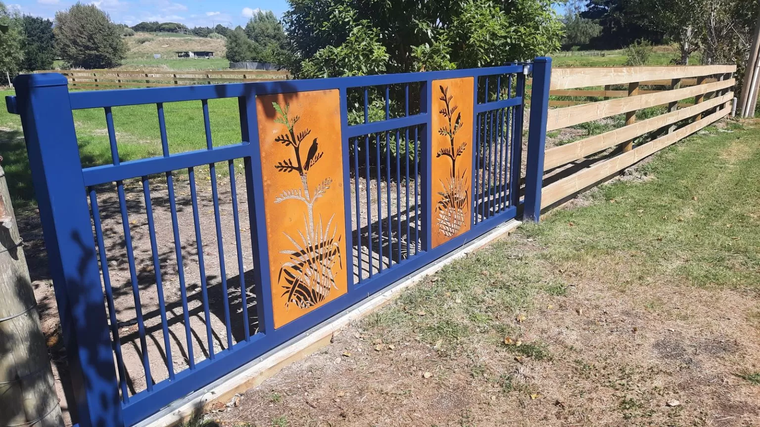 Blue powder-coated aluminium gate with Corten flax panels on a rural fence line