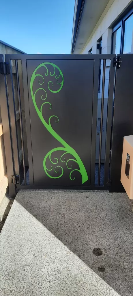 Black aluminium pedestrian gate with a green laser-cut koru design