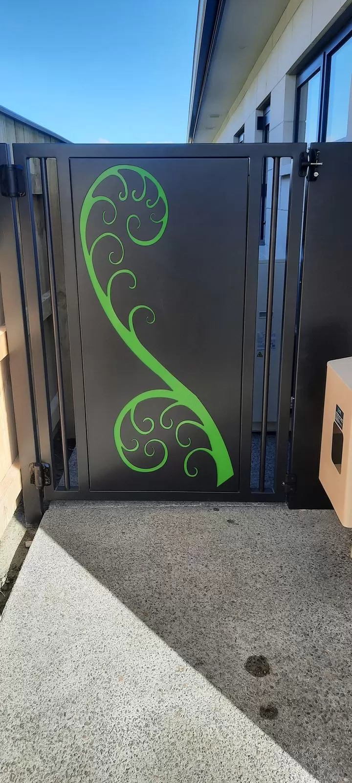 Black aluminium pedestrian gate with a green laser-cut koru design