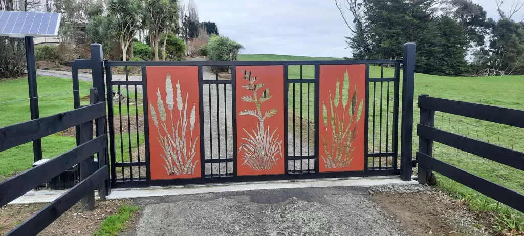 Black aluminium sliding driveway gate with three custom powder-coated panels on a rural property
