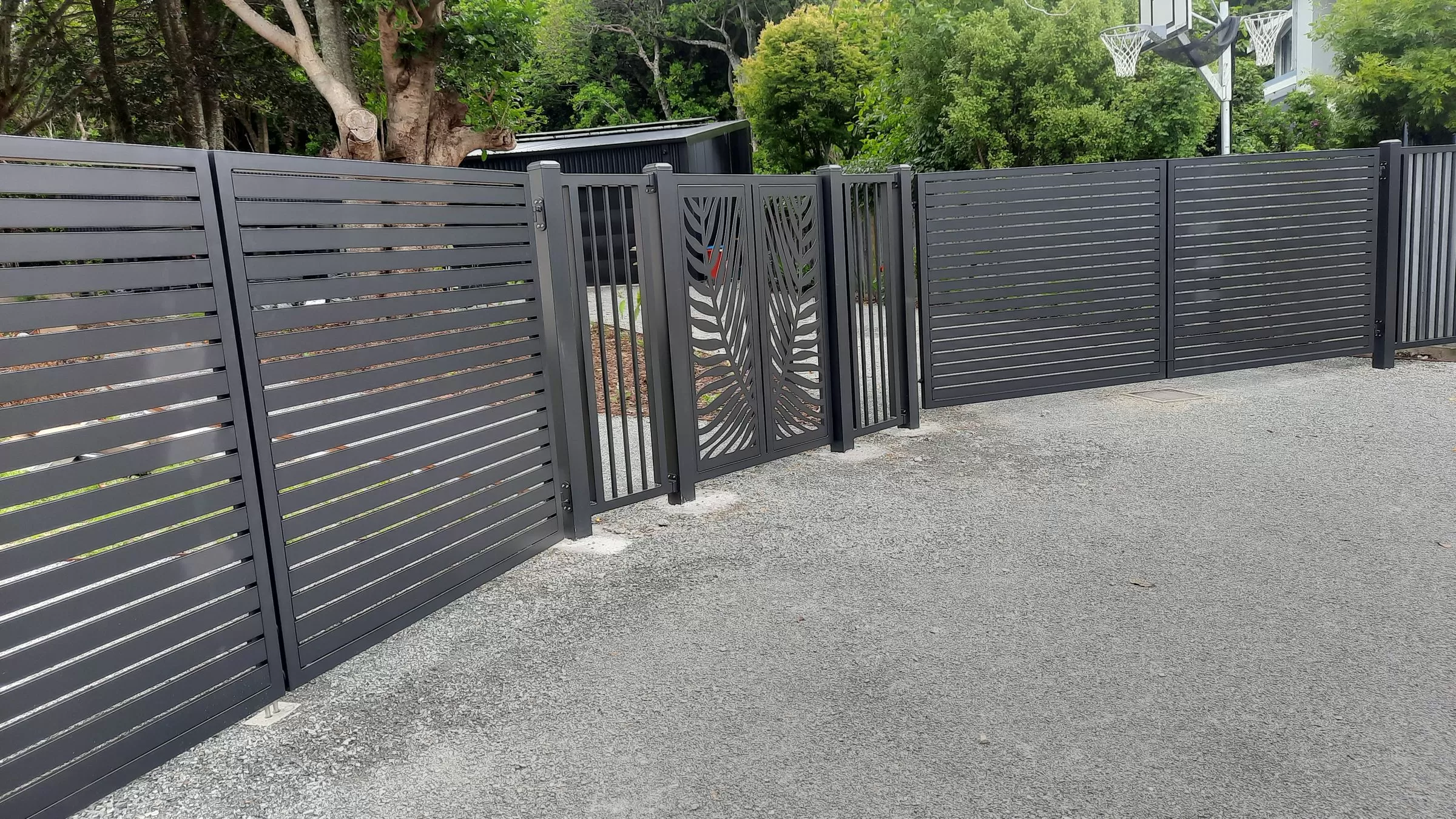 Full property frontage with charcoal aluminium slat fencing, driveway gates and a pedestrian gate